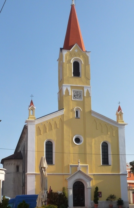 Slika je okomita te je na njoj prikazana prednja strana crkve Svetog Zenona. Crkva je žute boje, dok je renovirani zvonik narančaste boje.